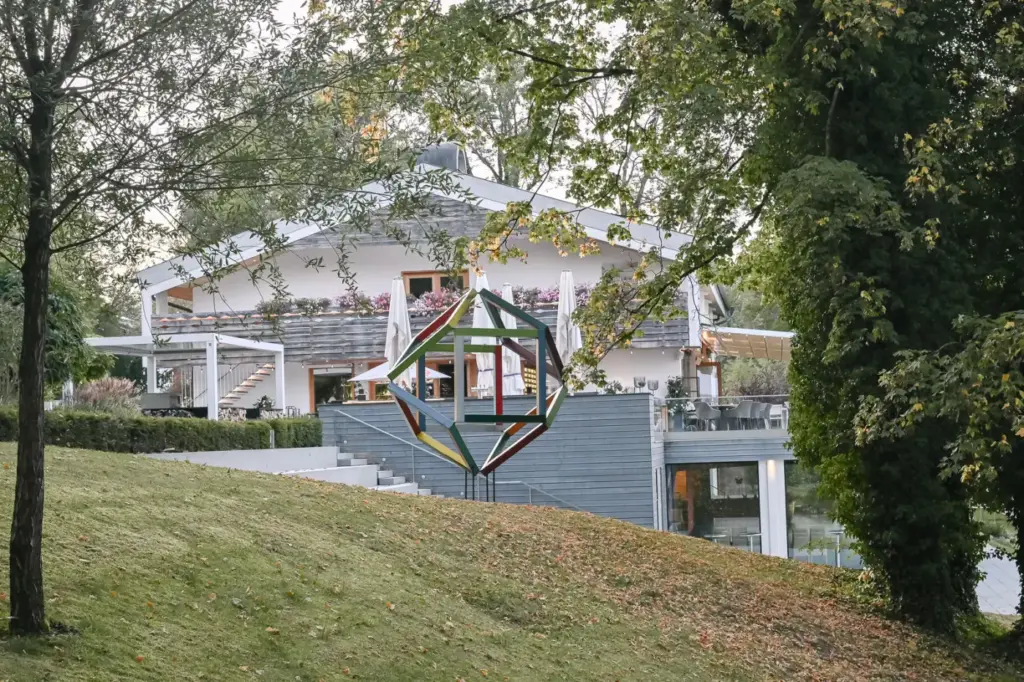 Das Marina Hotel am Yachthafen Bernried von unten gesehen, davor eine bunte Skulptur auf der Wiese, dahinter die Terrasse