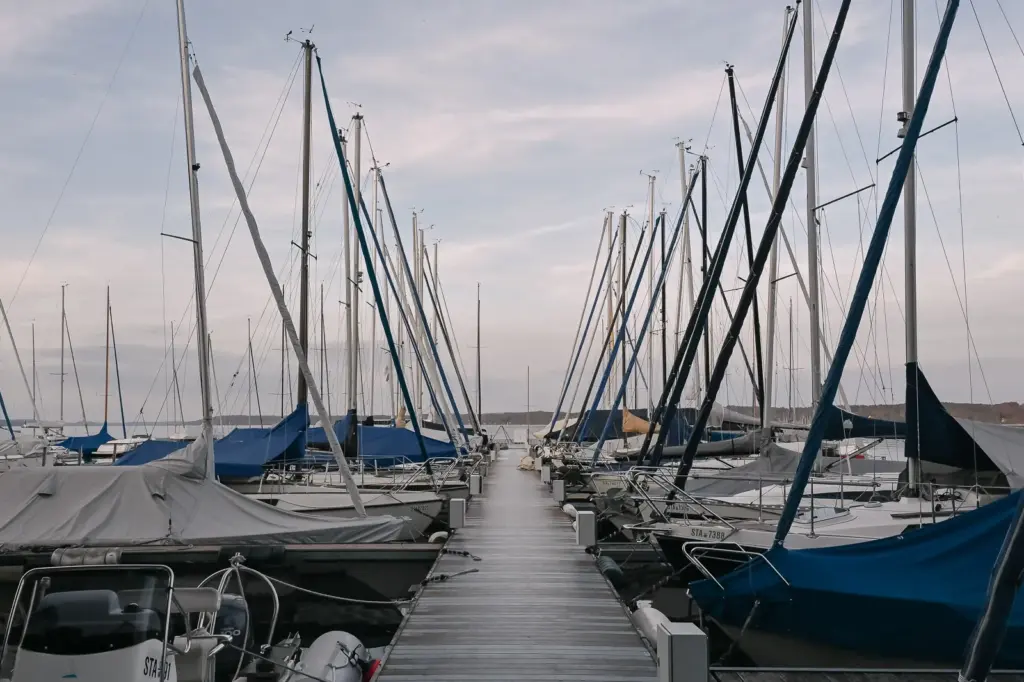 Blick von einem Steg im Yachthafen Bernried auf den See, links und rechts liegen Segelboote mit Planen