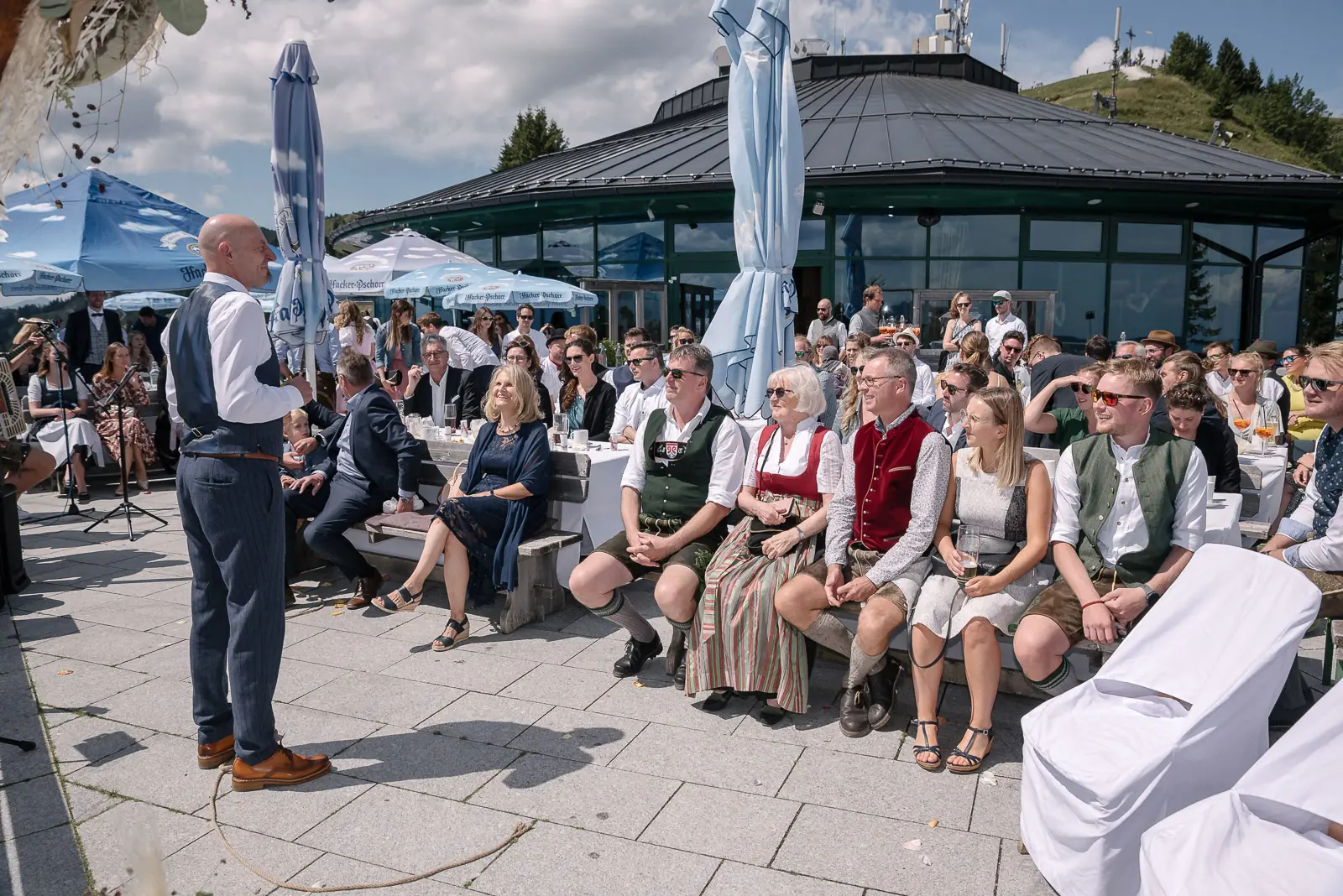 Gäste sitzen auf der Terrasse des Panoramarestaurants, davor steht ein Mann und spricht