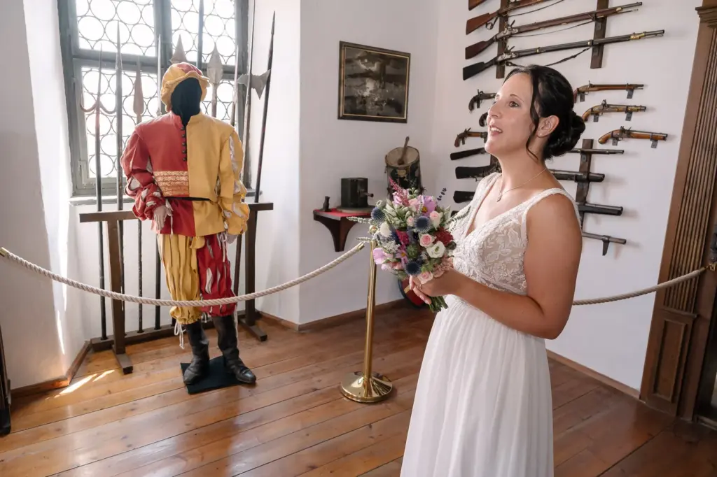 Braut mit Brautstrauß in einem Museumsraum mit historischen Waffen und einer bunten Figur