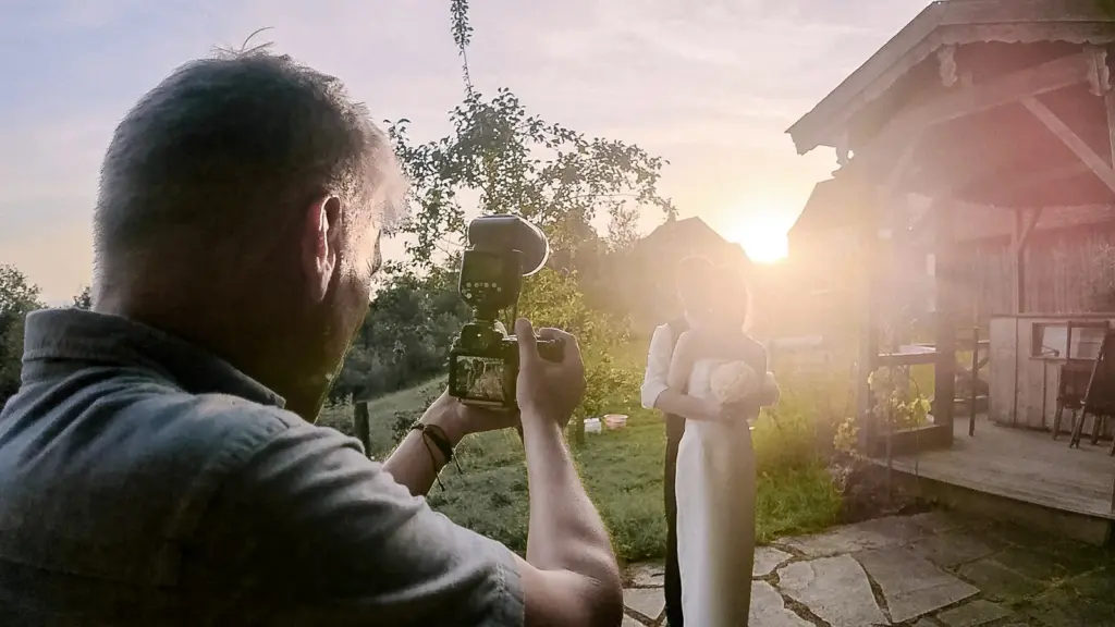 Harry Wolfsbauer fotografiert bei einer Hochzeit im Gegenlicht der Abendsonne das Brautpaar, daneben eine Holzhütte