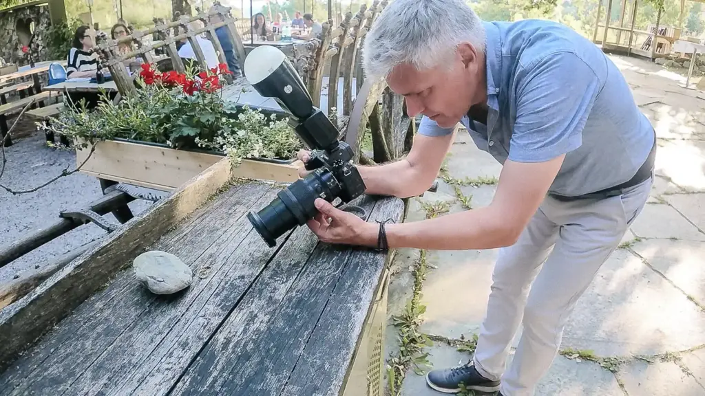 Harry Wolfsbauer beugt sich bei einer Hochzeit im Moarwirt mit Kamera und Aufsteckblitz über zwei Eheringe auf einem Holztisch