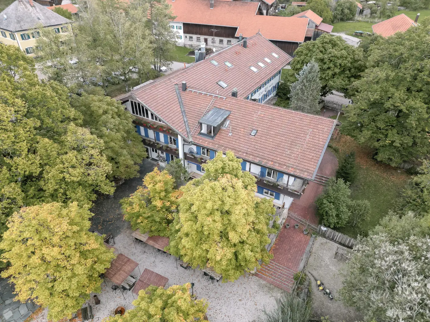 Luftaufnahme des Moarwirts in Hechenberg mit rotem Ziegeldach, davor ein Garten mit Sitzplätzen unter großen Bäumen