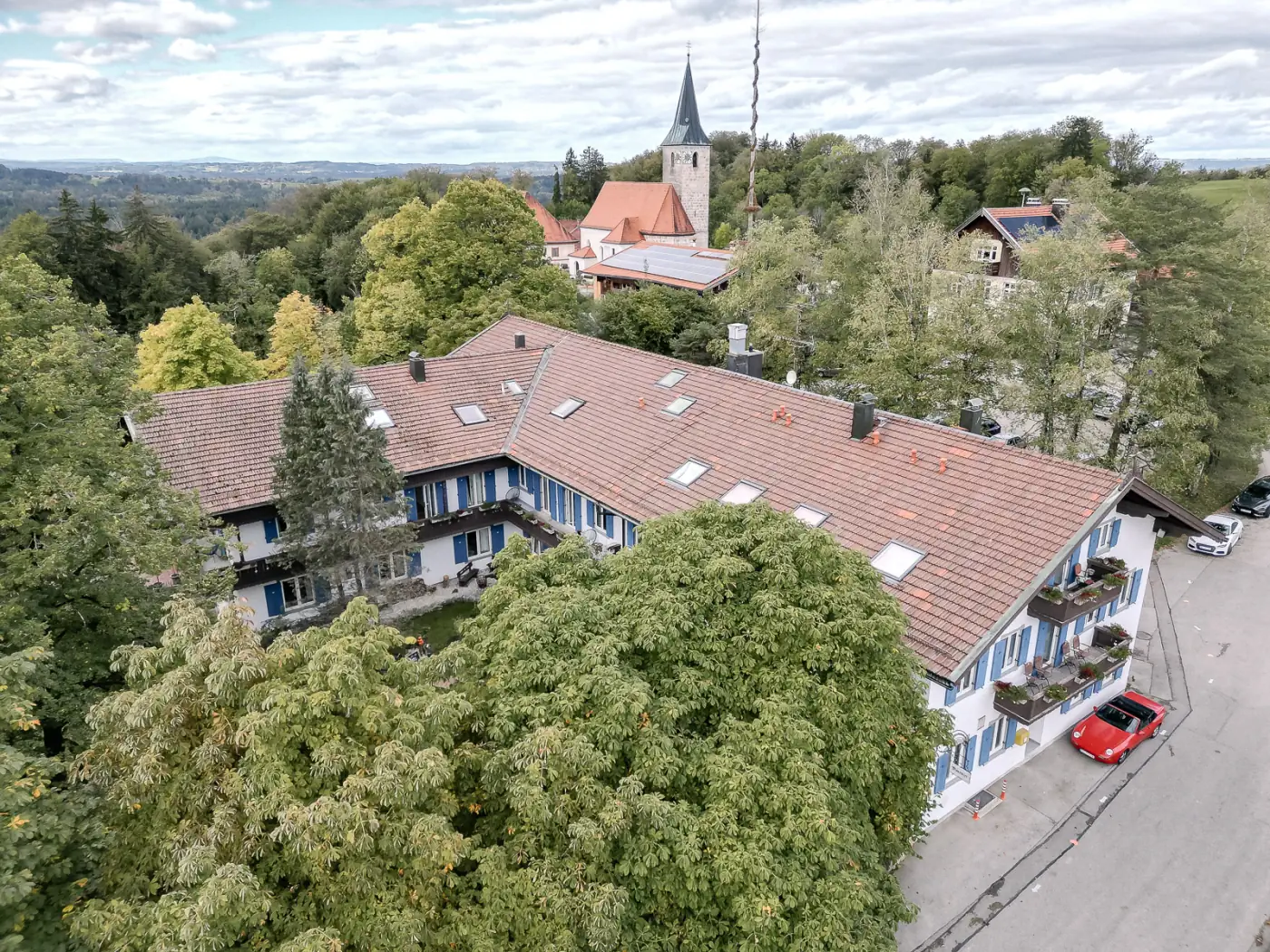 Luftaufnahme des Moarwirts in Hechenberg mit dem Satteldach des Gasthofs, im Hintergrund die Kirche St. Valentin