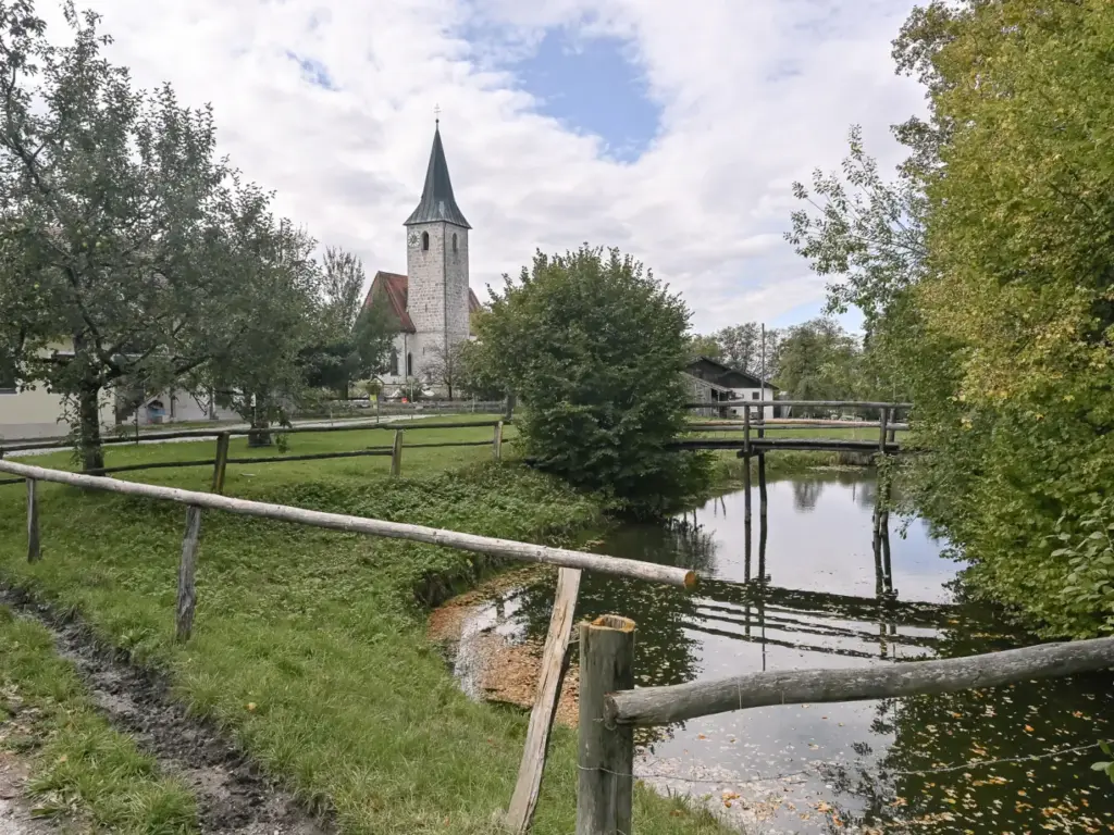 Blick über den Weiher auf die Holzbrücke, im Hintergrund der Turm der Kirche St. Valentin