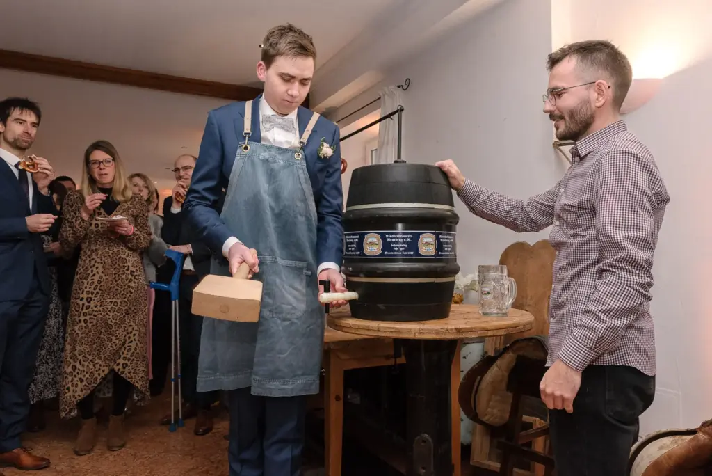 Bräutigam in Schürze schlägt mit einem Holzhammer den Zapfhahn in ein Bierfass