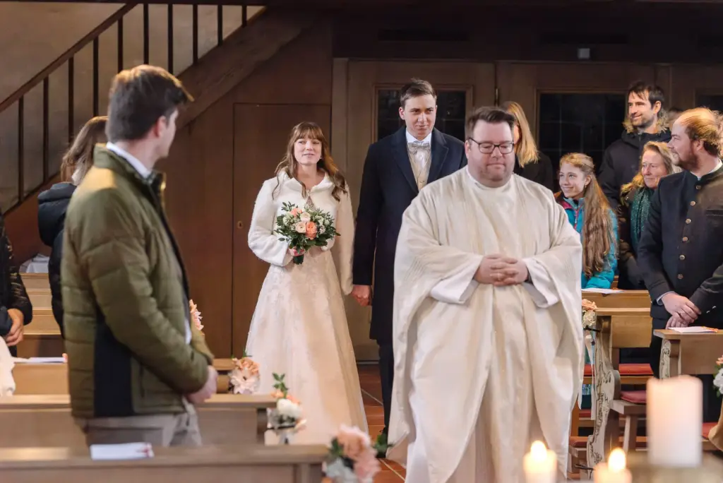 Braut und Bräutigam gehen hinter dem Pfarrer durch den Mittelgang der Kirche