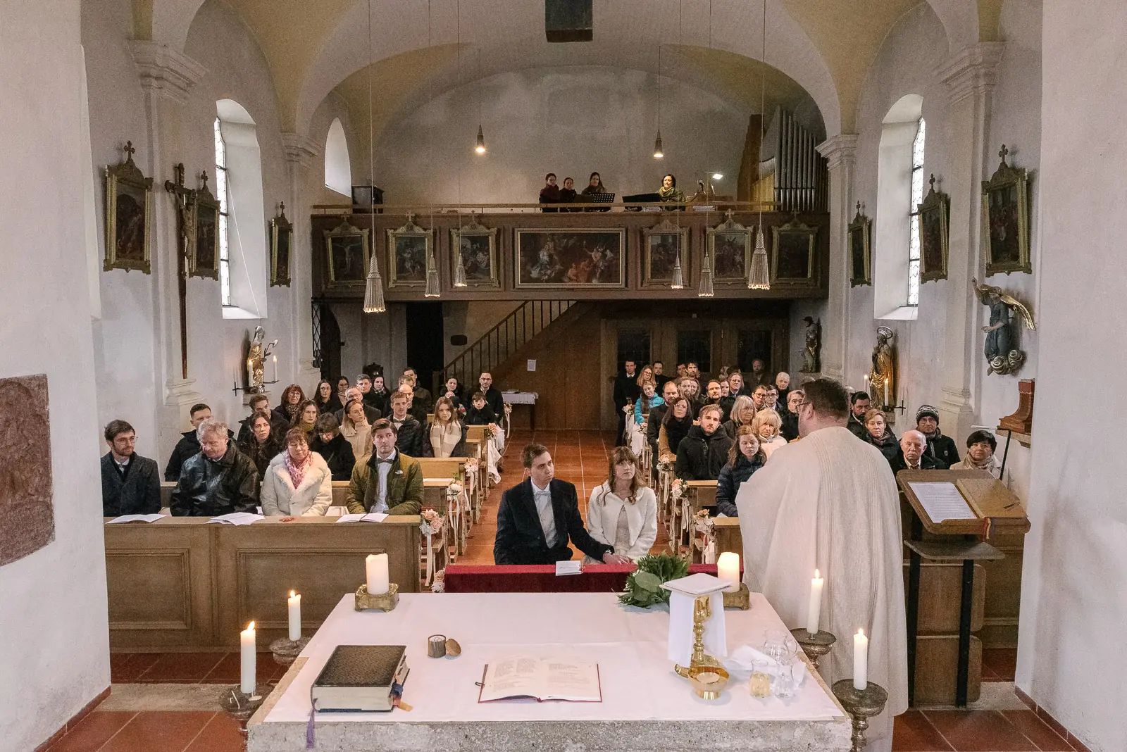 Blick in die Kirche: Brautpaar vor dem Altar, Pfarrer und Gäste in den Bänken, oben auf der Empore Musiker