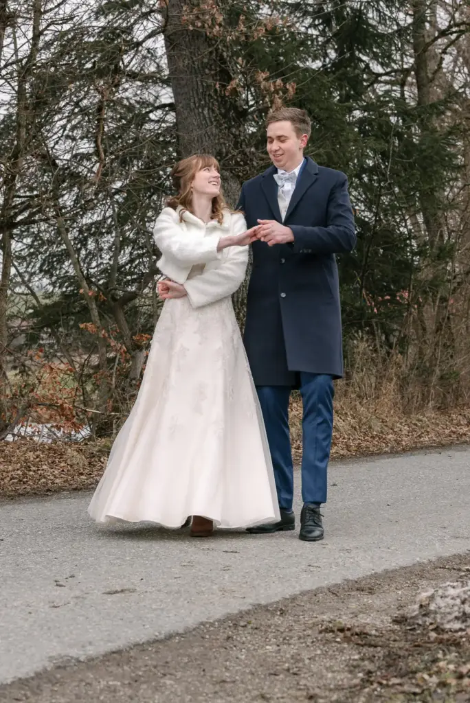 Brautpaar steht Hand in Hand auf einem Weg vor Bäumen